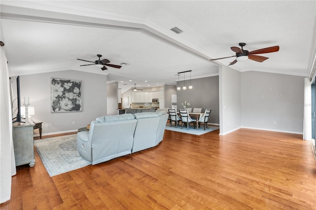 living room featuring vaulted ceiling, ornamental molding, light wood finished floors, and visible vents