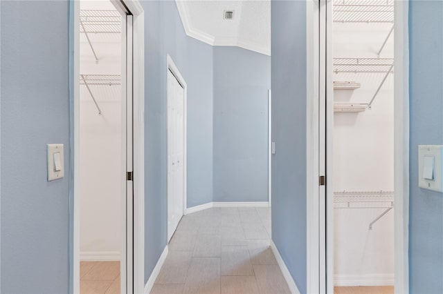 hallway with light tile patterned floors, a textured ceiling, visible vents, baseboards, and ornamental molding