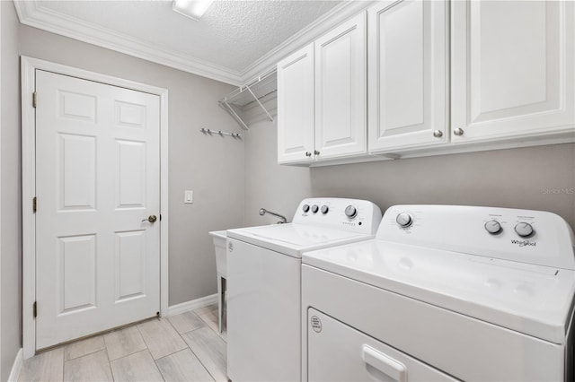 clothes washing area with crown molding, cabinet space, a textured ceiling, washer and dryer, and baseboards