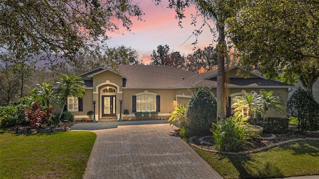 mediterranean / spanish-style house with a front yard, decorative driveway, and stucco siding