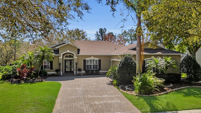 mediterranean / spanish-style house featuring decorative driveway, a front yard, and stucco siding