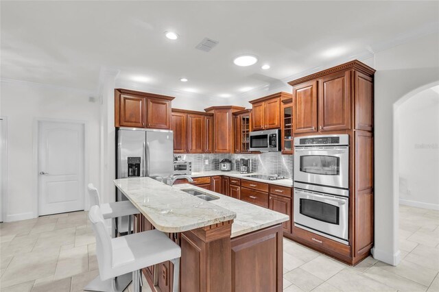 kitchen with a center island with sink, stainless steel appliances, backsplash, a sink, and a kitchen bar