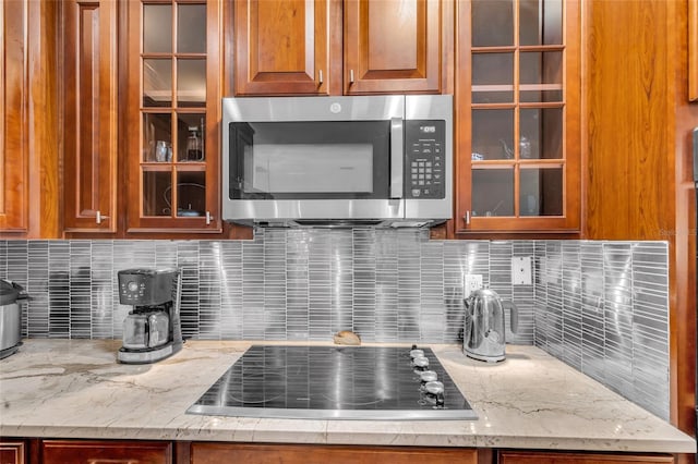 kitchen featuring glass insert cabinets, light stone countertops, stainless steel microwave, and black electric cooktop