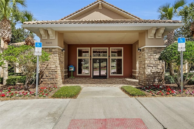 entrance to property with stone siding, a tile roof, and stucco siding