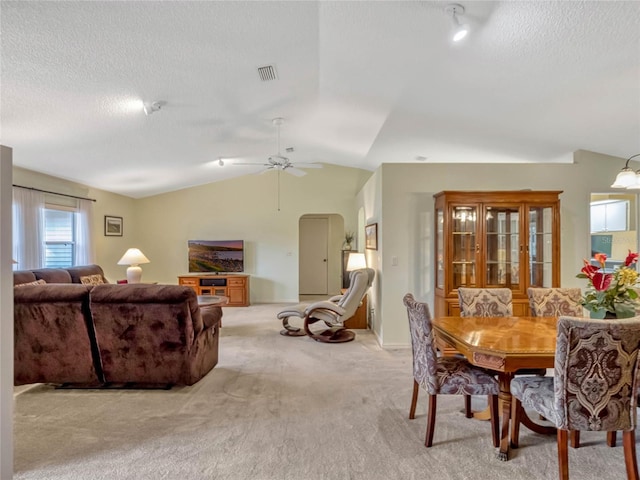 dining room featuring arched walkways, visible vents, light carpet, vaulted ceiling, and a textured ceiling