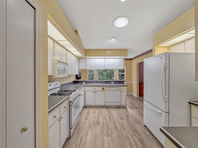 kitchen with white appliances, white cabinets, dark countertops, light wood-style flooring, and a sink