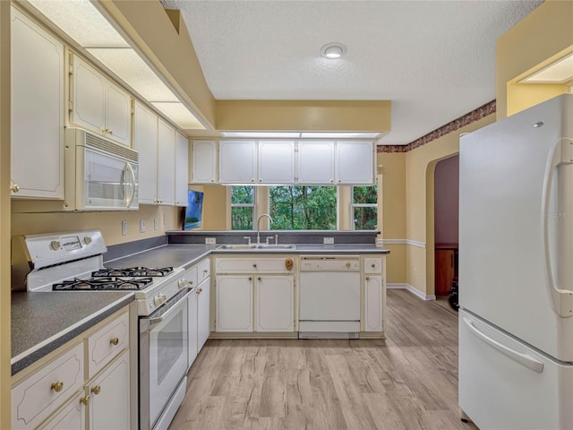 kitchen with a peninsula, white appliances, a sink, white cabinets, and dark countertops