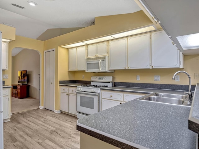 kitchen featuring arched walkways, dark countertops, visible vents, a sink, and white appliances