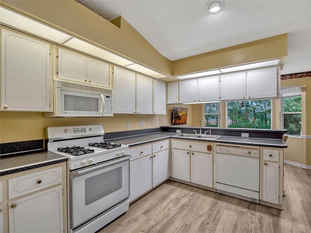 kitchen featuring dark countertops, white cabinetry, a sink, white appliances, and a peninsula