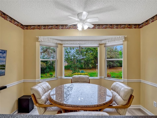 dining area with light wood-type flooring, baseboards, a ceiling fan, and a textured ceiling