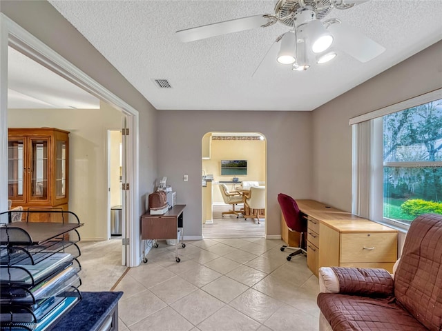 office area with visible vents, arched walkways, a ceiling fan, a textured ceiling, and light tile patterned flooring