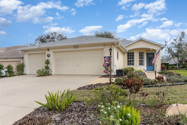 ranch-style home with a shingled roof, concrete driveway, an attached garage, central air condition unit, and stucco siding