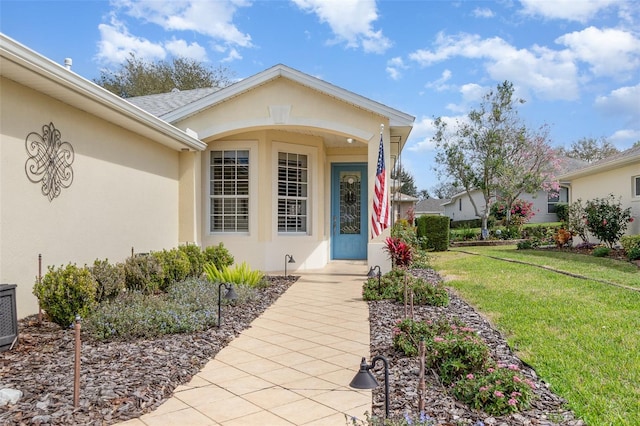 view of exterior entry featuring a lawn and stucco siding