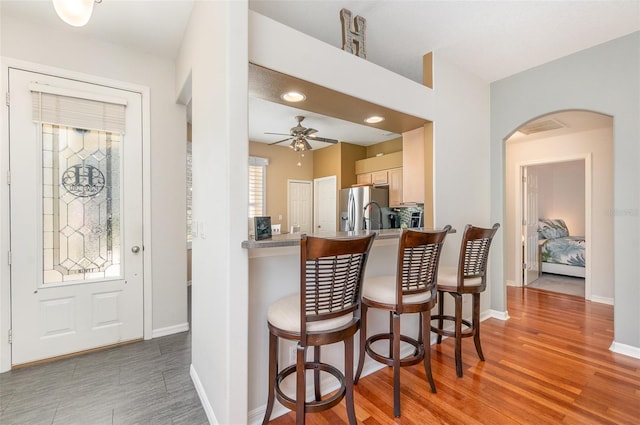 kitchen with stainless steel fridge, arched walkways, baseboards, light wood-type flooring, and a kitchen bar