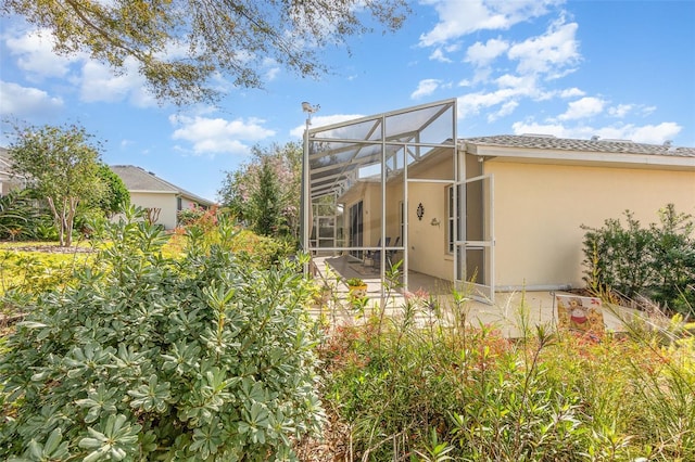 rear view of property featuring glass enclosure, a patio, and stucco siding