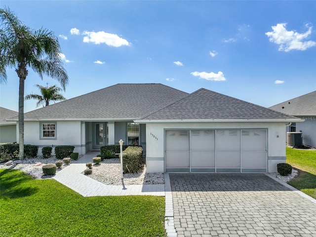 ranch-style home featuring decorative driveway, stucco siding, central air condition unit, an attached garage, and a front lawn