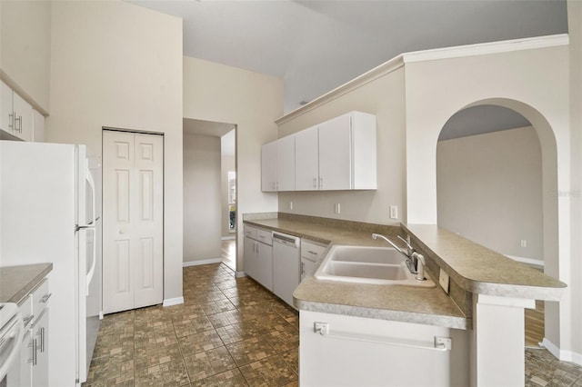 kitchen with a peninsula, white appliances, a sink, baseboards, and white cabinets