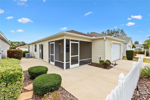 back of house with concrete driveway, an attached garage, a sunroom, central AC, and fence