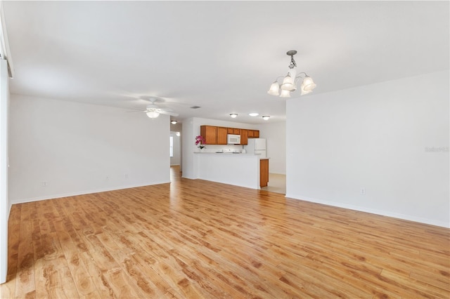 unfurnished living room featuring ceiling fan with notable chandelier, light wood-style flooring, and baseboards