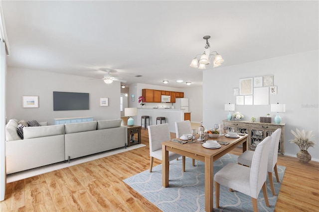 dining room featuring ceiling fan with notable chandelier, light wood finished floors, and baseboards