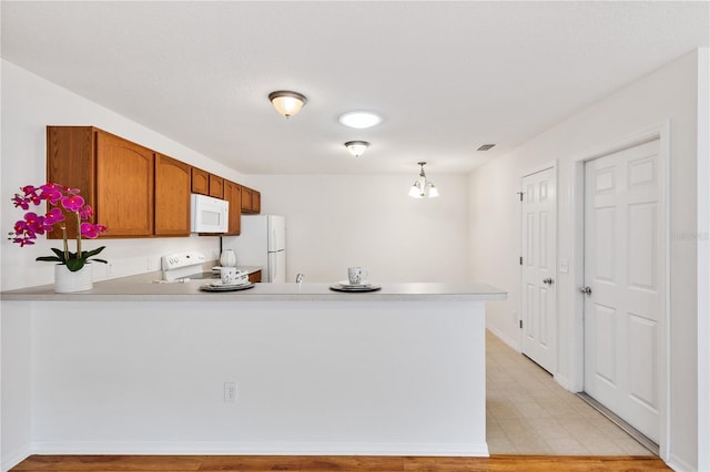 kitchen featuring white appliances, brown cabinetry, a peninsula, light countertops, and pendant lighting