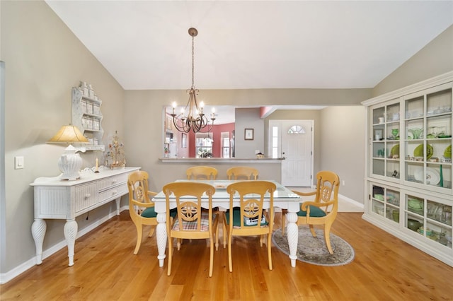 dining room featuring light wood-type flooring, baseboards, a chandelier, and lofted ceiling