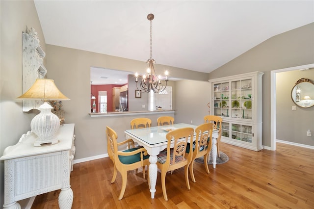 dining space featuring light wood-type flooring, baseboards, vaulted ceiling, and a notable chandelier