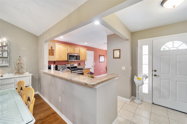 kitchen featuring light stone counters, light brown cabinetry, appliances with stainless steel finishes, a peninsula, and baseboards