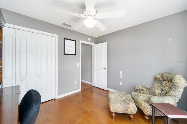 living area with a ceiling fan, wood finished floors, visible vents, and baseboards