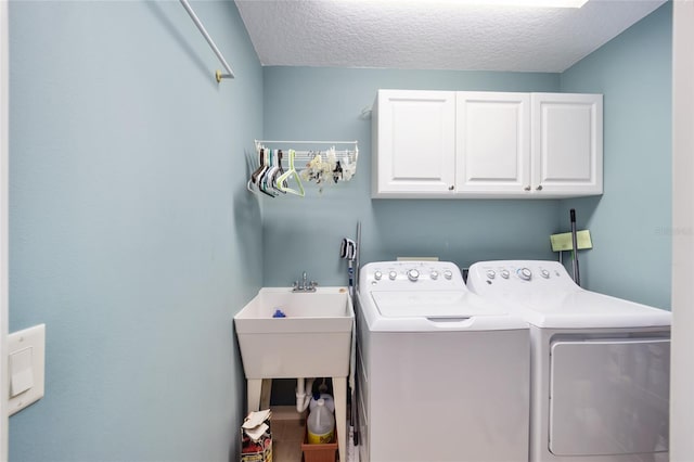 clothes washing area with washing machine and dryer, cabinet space, and a textured ceiling