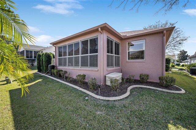 view of side of home with a sunroom, central AC, a lawn, and stucco siding