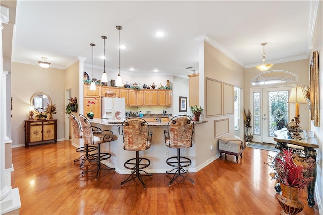 kitchen with a breakfast bar area, a peninsula, ornamental molding, white fridge with ice dispenser, and light wood finished floors