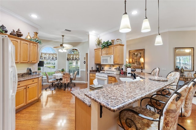 kitchen with light stone counters, white appliances, a sink, light wood finished floors, and a kitchen bar