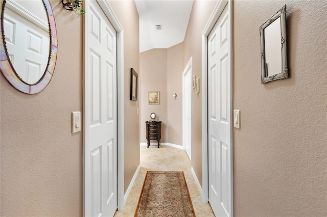 hall featuring light tile patterned flooring, visible vents, and baseboards