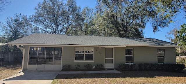 ranch-style home featuring concrete driveway, roof with shingles, and fence