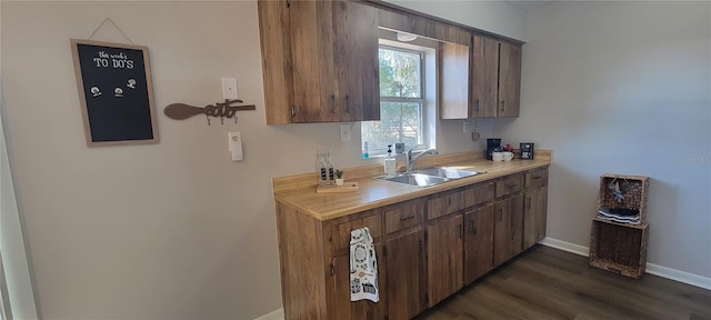 kitchen featuring light countertops, a sink, dark wood finished floors, and baseboards