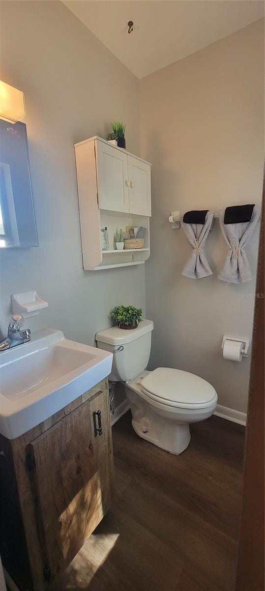 half bath with baseboards, toilet, wood finished floors, vaulted ceiling, and vanity