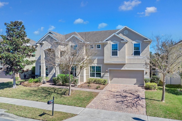 traditional-style home featuring a garage, a front yard, decorative driveway, and stucco siding