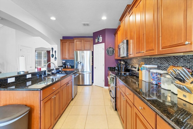 kitchen featuring appliances with stainless steel finishes, brown cabinetry, dark stone countertops, and a sink