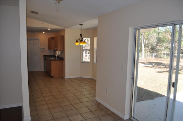 kitchen with pendant lighting, brown cabinets, dark countertops, lofted ceiling, and light tile patterned flooring