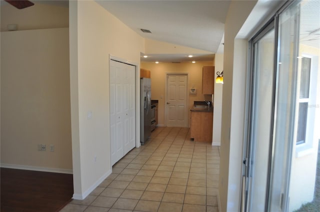 hall with visible vents, vaulted ceiling, baseboards, and light tile patterned floors