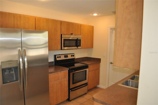 kitchen with dark countertops, light tile patterned floors, appliances with stainless steel finishes, and a sink