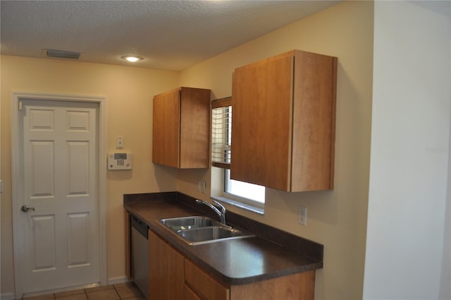 kitchen featuring visible vents, dark countertops, brown cabinets, a sink, and stainless steel dishwasher