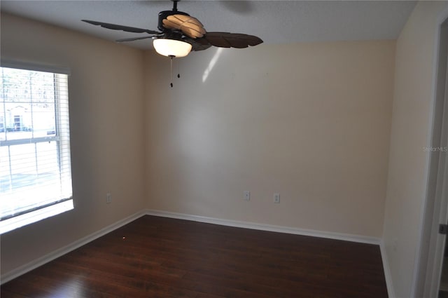 empty room with dark wood finished floors, a ceiling fan, and baseboards