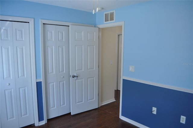 unfurnished bedroom featuring multiple closets, baseboards, visible vents, and dark wood-type flooring