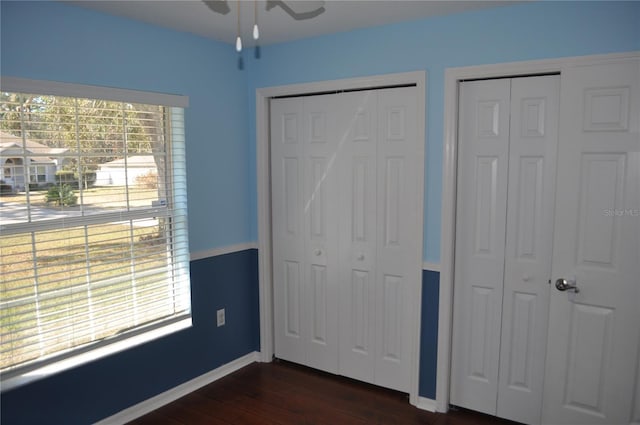 unfurnished bedroom featuring dark wood-type flooring, ceiling fan, baseboards, and two closets