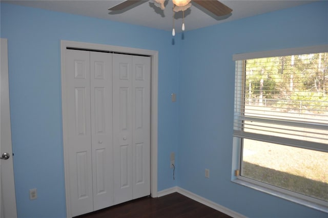 unfurnished bedroom featuring a closet, dark wood finished floors, a ceiling fan, and baseboards