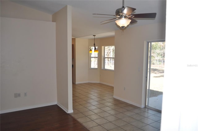 empty room featuring ceiling fan with notable chandelier, baseboards, and light tile patterned flooring