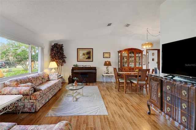 12338 S Putney Ct, Leesburg, FL 34788 - living room featuring lofted ceiling, visible vents, light wood-style flooring, a textured ceiling, and a chandelier