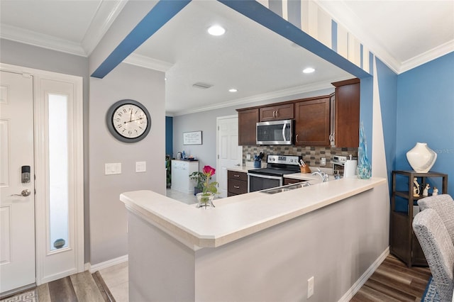 kitchen with appliances with stainless steel finishes, a peninsula, light countertops, crown molding, and a sink